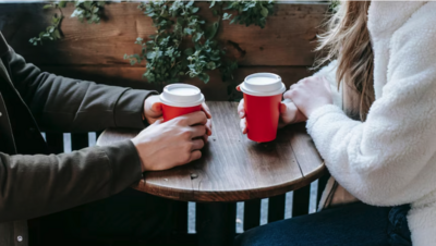 Couple facing each other at a table drinking takeaway coffee and talking – representing relationship support and couples counselling with Freedom Couple Counselling in Melbourne.