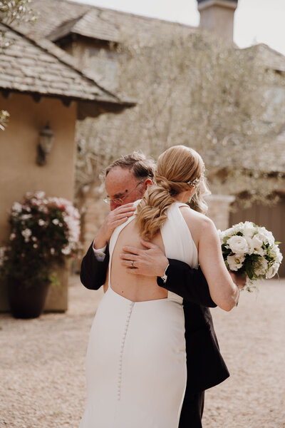 Bride and father hug in front of Mediterranean house