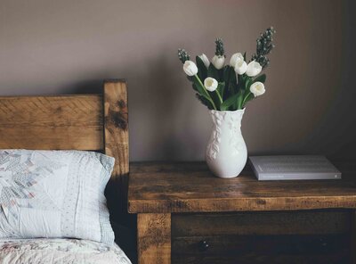 Wooden bed frame and nightstand with white vase and white tulips