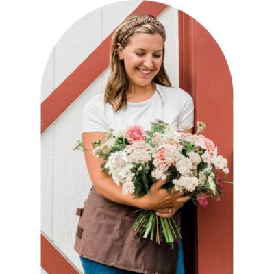 Woman in front of a barn looking at a bouquet of flowers and smiling