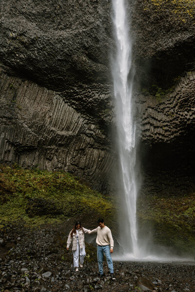 Couple exploring beneath a waterfall in Oregon, showcasing outdoor adventure elopement packages