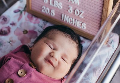 Newborn baby girl in a pink outfit resting in a hospital bassinet, showcasing her delicate features and peaceful expression.