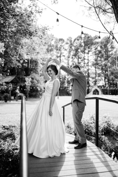 little rock wedding photographers capture groom twirling his bride as they dance together on a bridge for their outdoor wedding