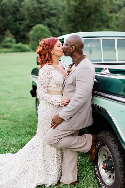 Wedding photo of a bride and groom kissing while leaning against a pickup truck for a portrait on their wedding day.