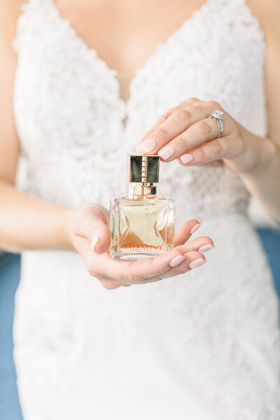Close up of bride delicately holding a gold tone Valentino perfume bottle