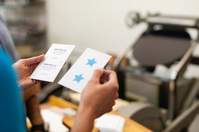 A designer's hands holding letterpress printed business cards with blue star.