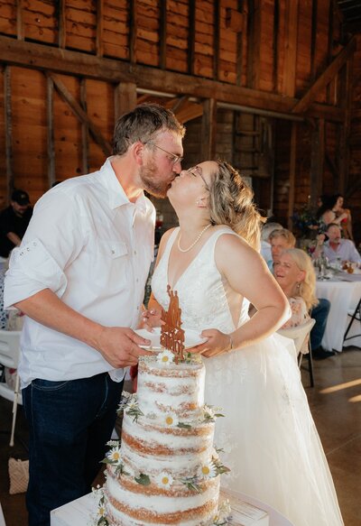 Bride and groom kissing behind their wedding cake
