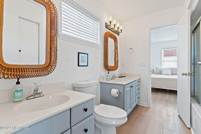 Master bathroom with light blue double vanities, chunky wooden mirrors, wrought iron vanity lights, and toilet centered between vanities.