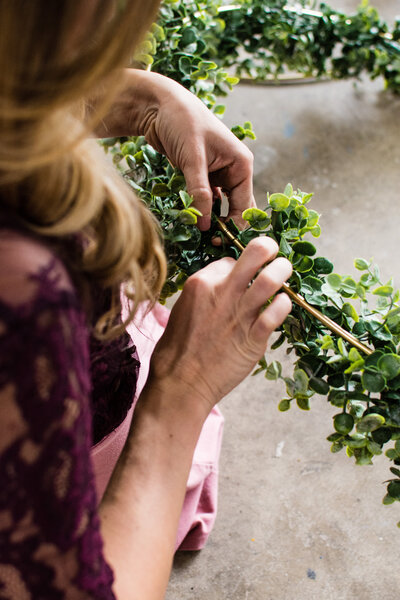 Close up of woman wrapping faux greenery around a gold hoop