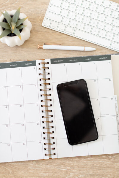 a smart phone sitting on top of a planner and desk stock image photography for the sales page for the bookkeeping template for creatives by Dolly DeLong Education
