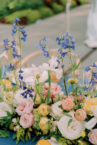 Blue, pink, yellow, and white flowers sit on a table.