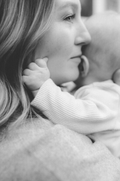 Close-up of a mother’s face as she holds her three-month-old son, who is turned away from the camera, captured in a tender film-style portrait by Emily Ambie.