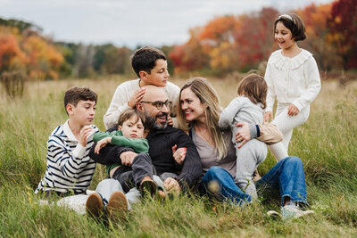 family snuggles with son on blanket in a field at sunset