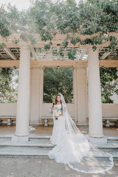 bride standing under pergola holding her wedding bouquet