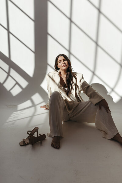 Keely of Riviera Creative sits on the floor in a cream suit casually looking at camera