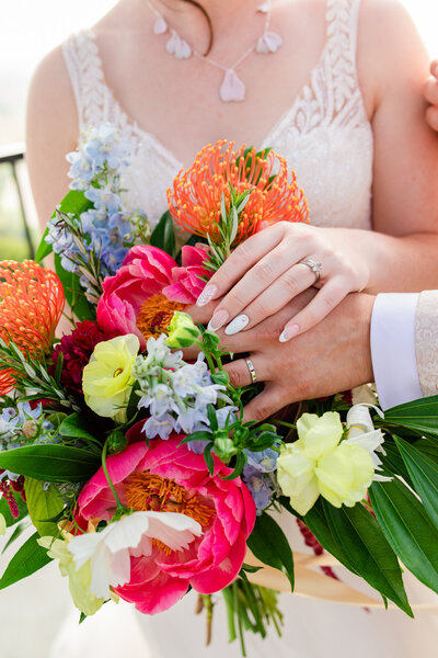 bride and groom show off rings on bouquet
