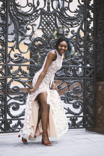 black woman in white long dress in front of ornate gate