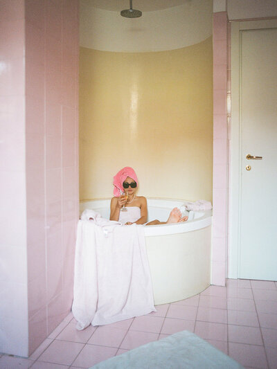 Bride in the bath at a hotel taken on film. She is wearing sunglasses and a towel on her head. Taken my Radostina Boseva