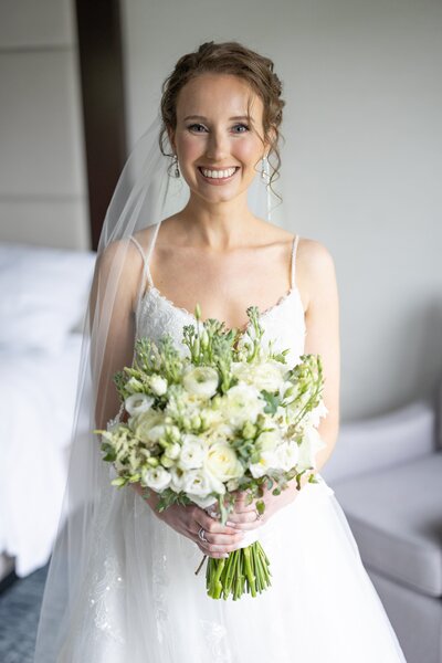 Bride standing in ballroom holding bridal bouquet looking out window