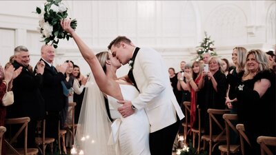 Bride and groom kiss walking down the aisle at the Broadway Avenue