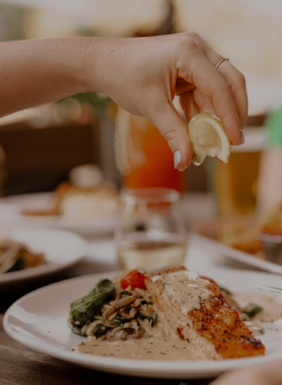 Plate of salmon with sauce and lemon wedge being squeezed over the fish