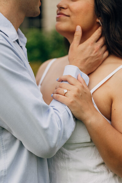 Engaged couple standing close, chest to chest, with a focus on the engagement ring.