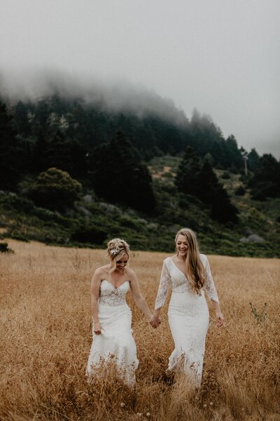 Two brides holding hands and walking through a field