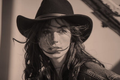 Young girl in a cowboy hat poses in the sun against a tractor.