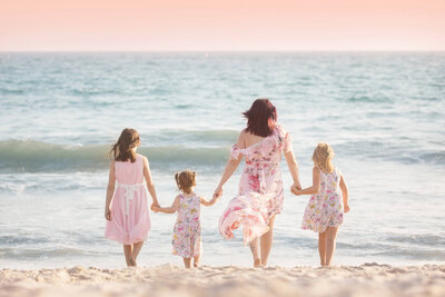 mom holding her three daughters hands and walking towards the water at sunset in Santa Monica