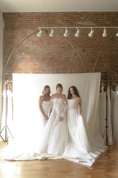 Three brides posing together in lace gowns.