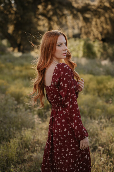 a girl with red hair poses in a field, a wedding and elopement photographer
