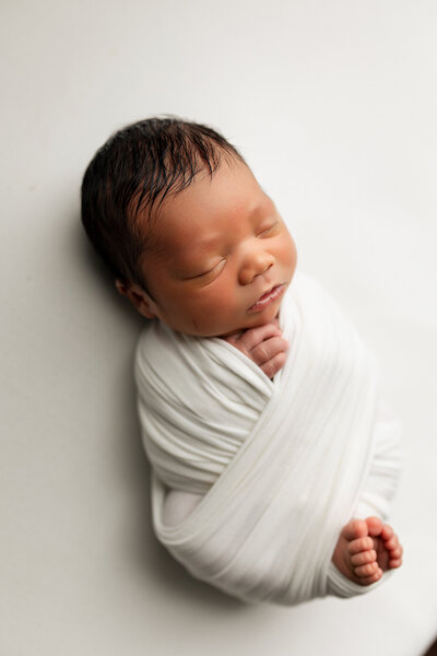 Newborn baby boy wrapped in white fabric.