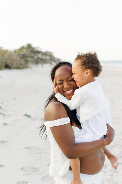 Daughter grabbing moms head and hugging her  on the beach during maternity photos