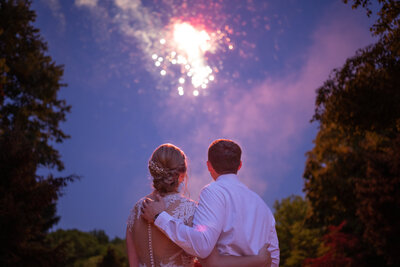 bride and groom hugs and embraces while taking in a surprise firework display during their intimate wedding reception. Aurora Ohio. Photo taken by Aaron Aldhizer