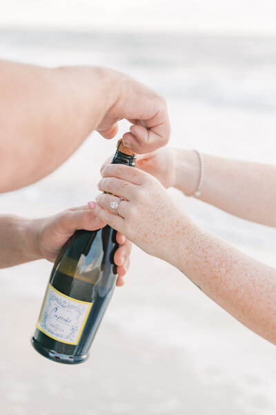 Close up of bride and groom opening bottle of champagne during engagement session