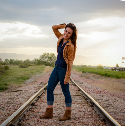 A woman poses in the middle of train tracks out in the middle of the country for a branding session.