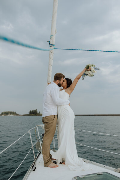bride and groom kissing on a sailboat. bride is holding her bouquet in the air