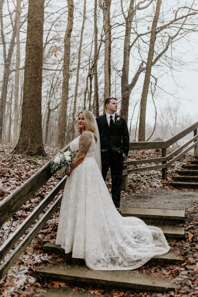A bride and groom pose on the steps while it's snowing