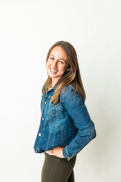 Woman in jean jackets has a hand on her hip and smiles at camera.