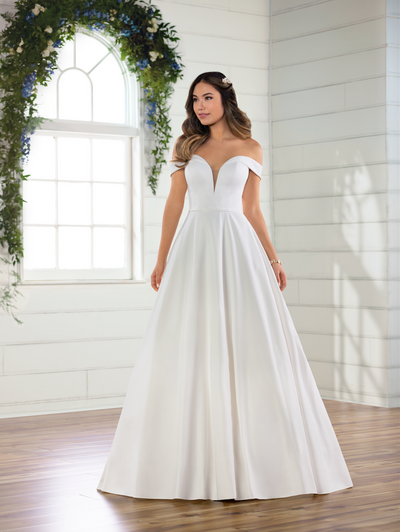 CLASSIC SATIN BALLGOWN WITH POCKETS AND OFF-THE-SHOULDER SLEEVES Clean and chic yet completely effortless, this fresh spin on the royal-inspired ballgown will leave you breathless. A classic satin ballgown, this silhouette features a plunging sweetheart neckline that seamlessly flows into banded off-the-shoulder straps, highlighting your neck and shoulders beautifully. Simple seaming highlights your frame throughout the grand silhouette, which floats out beneath the attached fabric waistband for a light finish. With modern pockets and traditional buttons running the length of the simple train, you’ll practically float down the aisle in this masterpiece for the dreaming romantic and modern minimalist. This gown is also available in plus sizes.