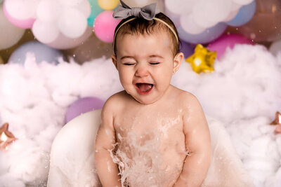 Portrait Photographers CT capture pure joy as baby laughs during bubble bath session with rainbow balloon garland