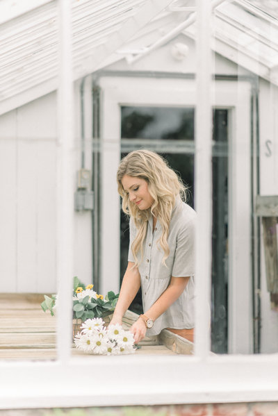 blonde girl in a greenhouse gardening and playing with white daisies