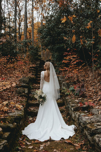 Bride standing in the middle of a fall covered forest holding her florals