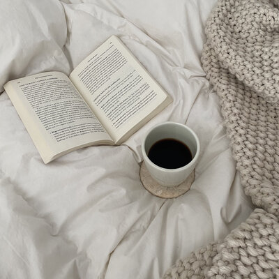 Open book and coffee mug sitting on top of cozy bedding