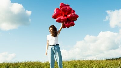 woman stood with red balloons smiling and looking confident