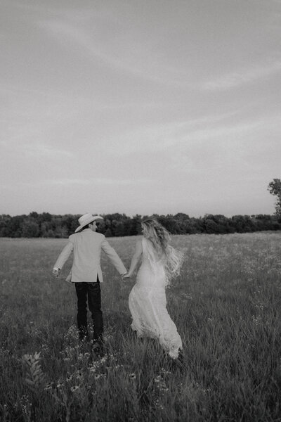 bride and groom run through the field together at their ranch wedding