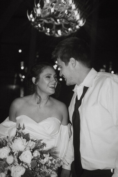 A black and white image of a couple smiling at each other on their wedding day