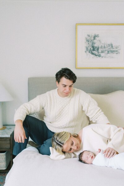 mom and dad sitting on bed gazing at baby