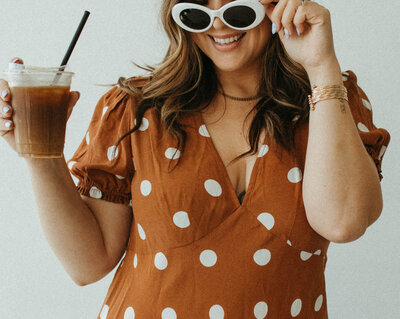 woman holding iced coffee smiling with sunglasses on
