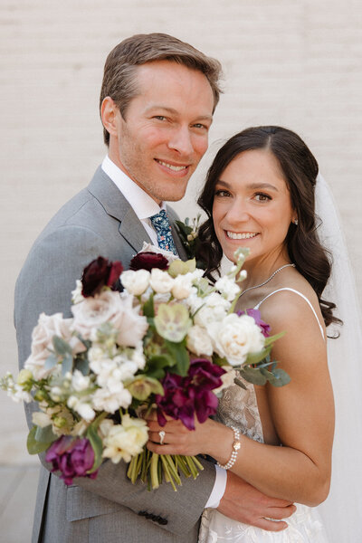 Brunette bride and blonde groom smiling at the camera for a wedding portrait outside of Wild Carrot in St. Louis